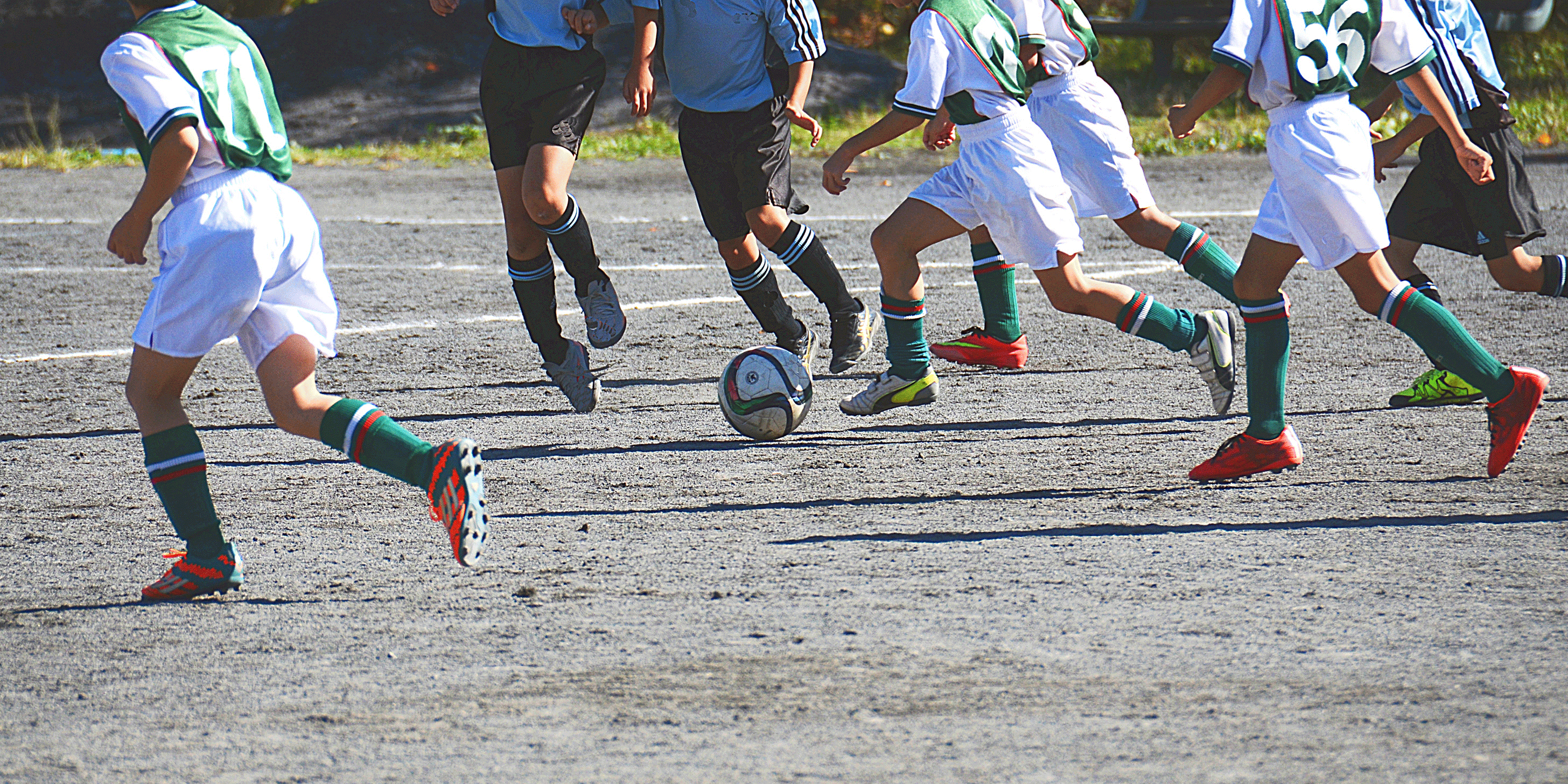 グラウンドでサッカーの試合をする少年たちの足元の画像